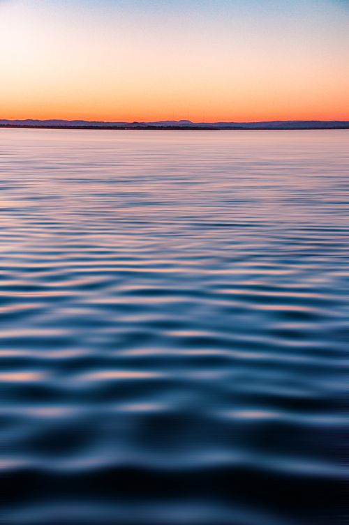Free Peaceful ocean view at twilight with calm water and soft ripples under a colorful sky. Stock Photo