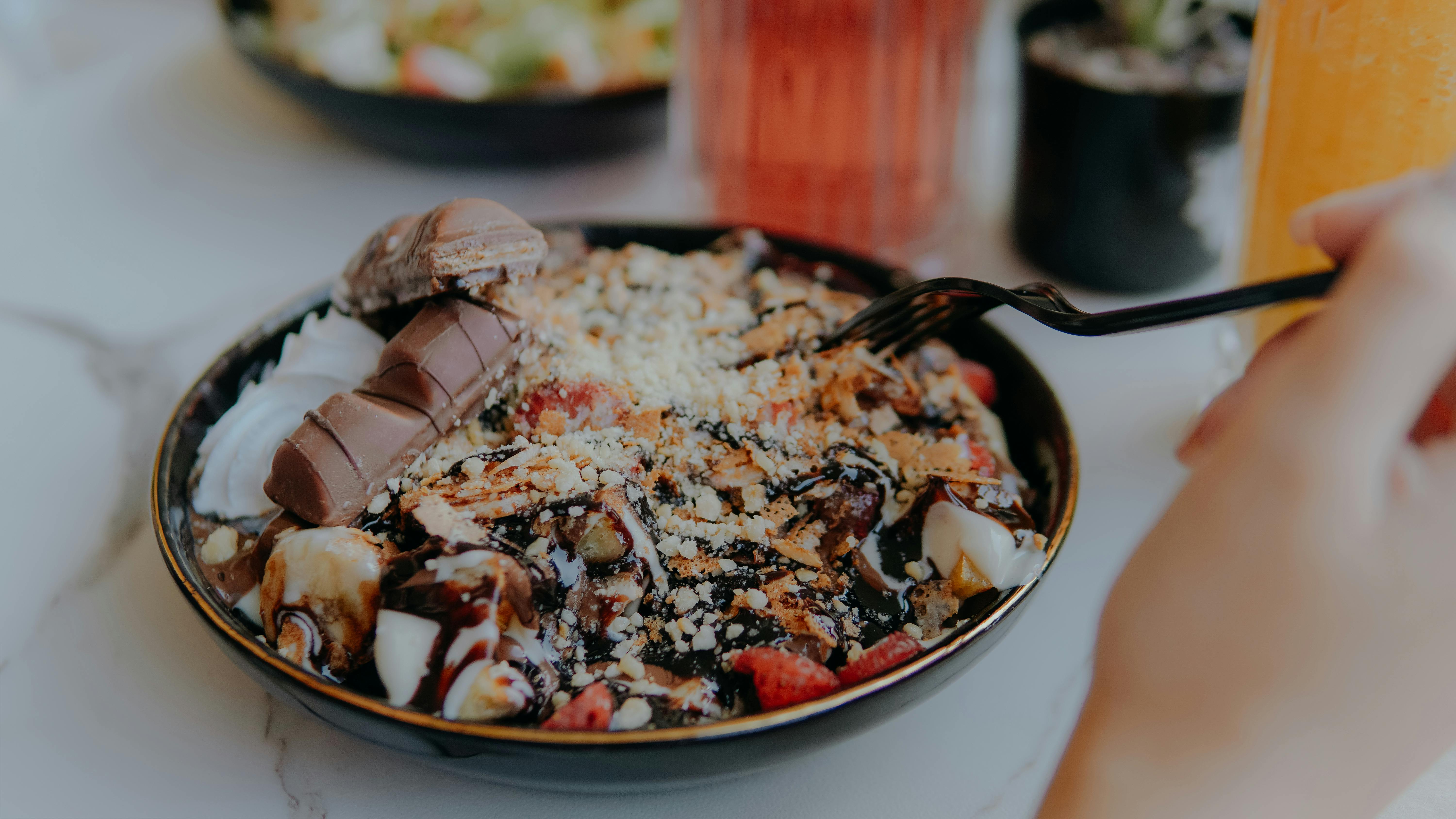 Close-up of a chocolate dessert bowl with slices of chocolate bar, fruits, and cream.