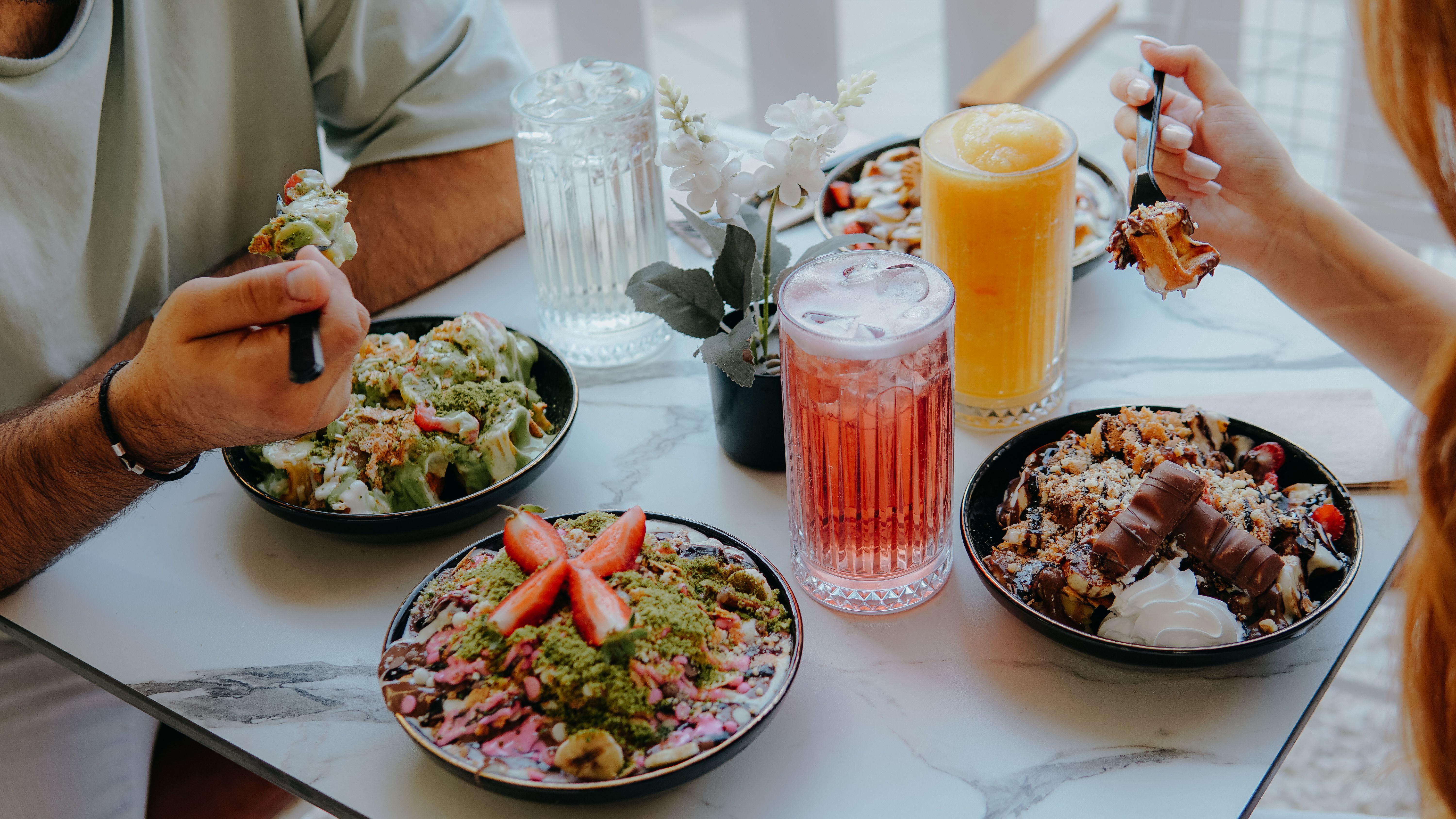 A vibrant brunch scene featuring assorted desserts and fresh smoothies enjoyed by two people indoors.