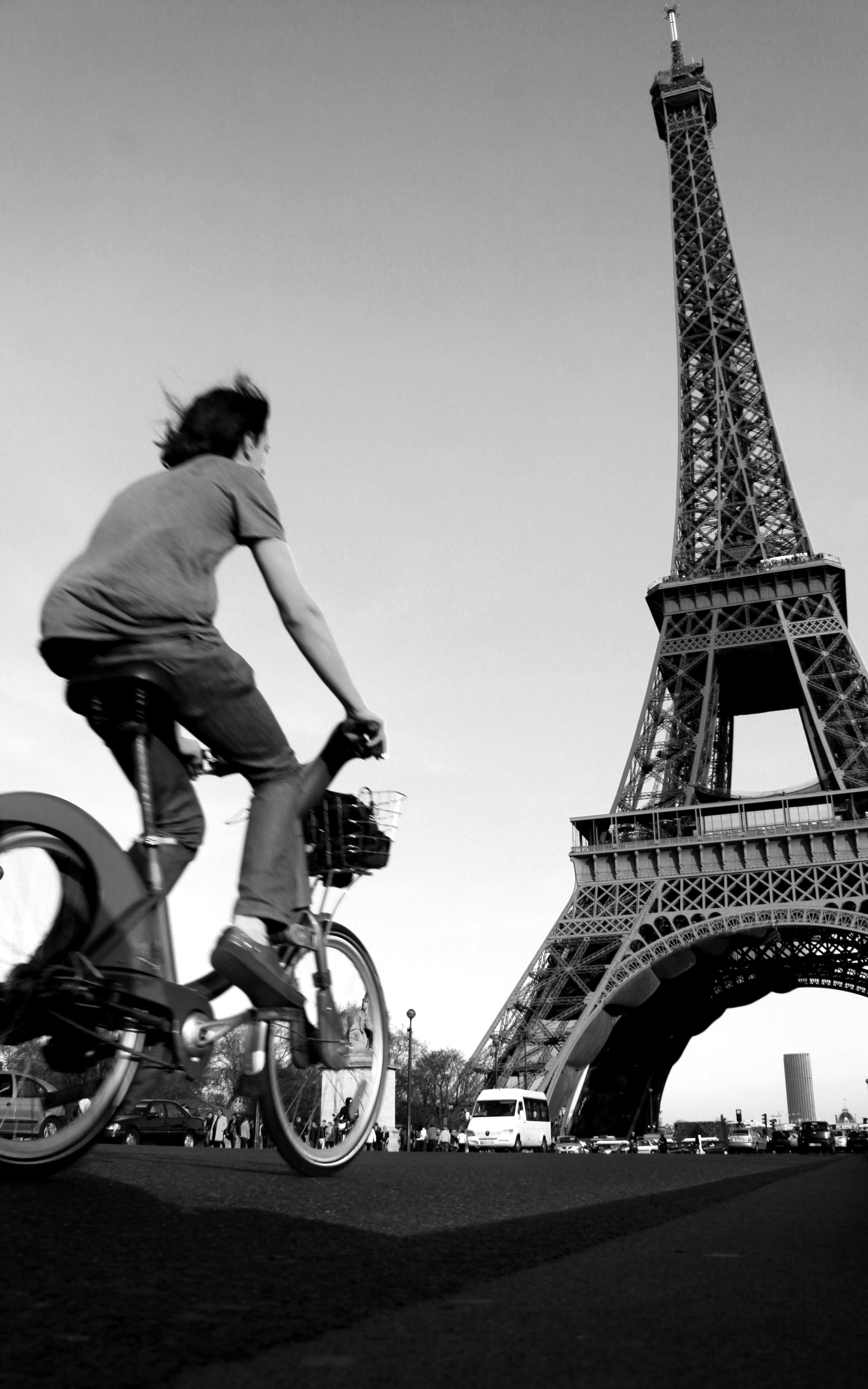 A cyclist rides near the iconic Eiffel Tower in a dynamic black and white photograph.