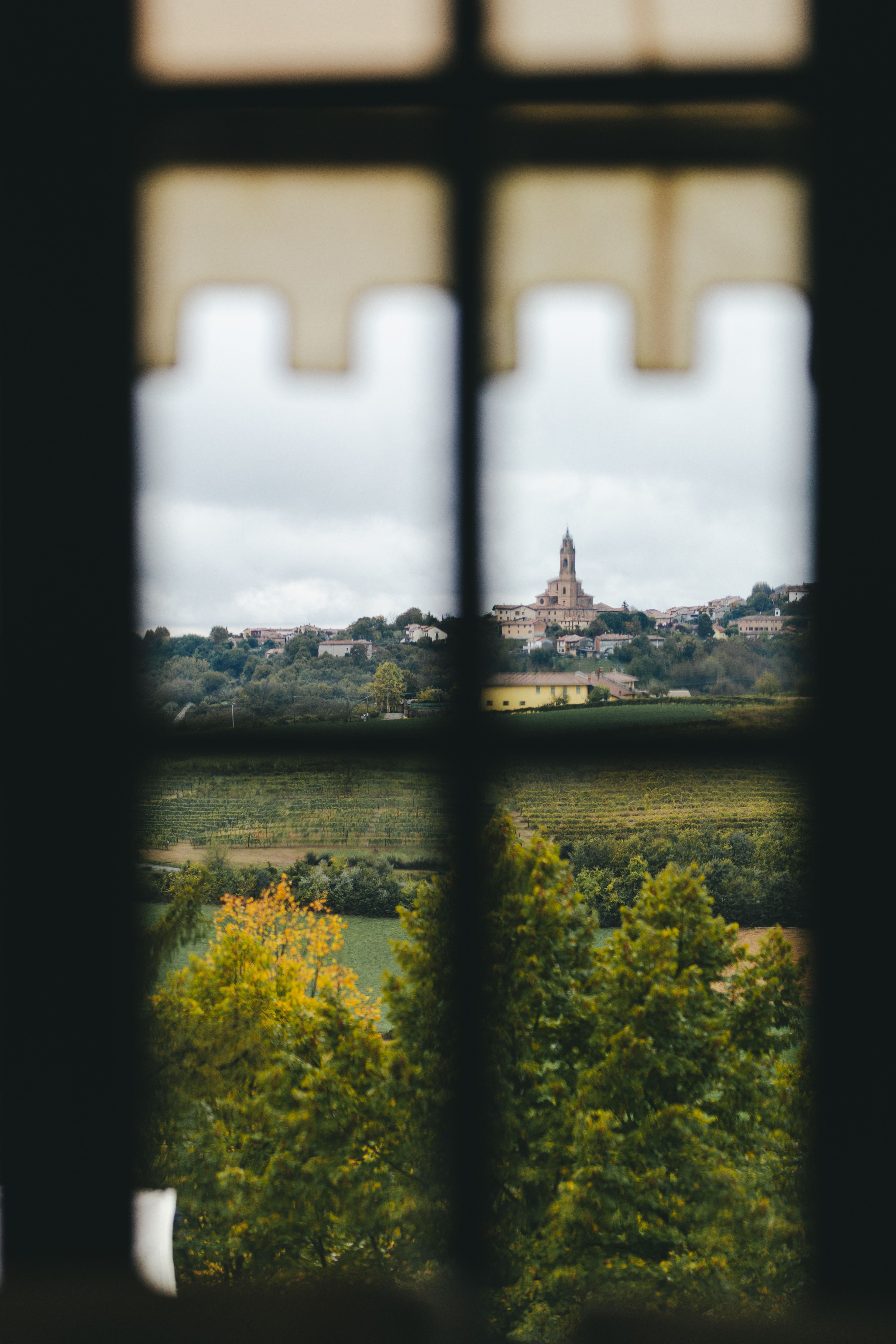 View of a picturesque European countryside through a window, featuring a historic town and lush landscape.