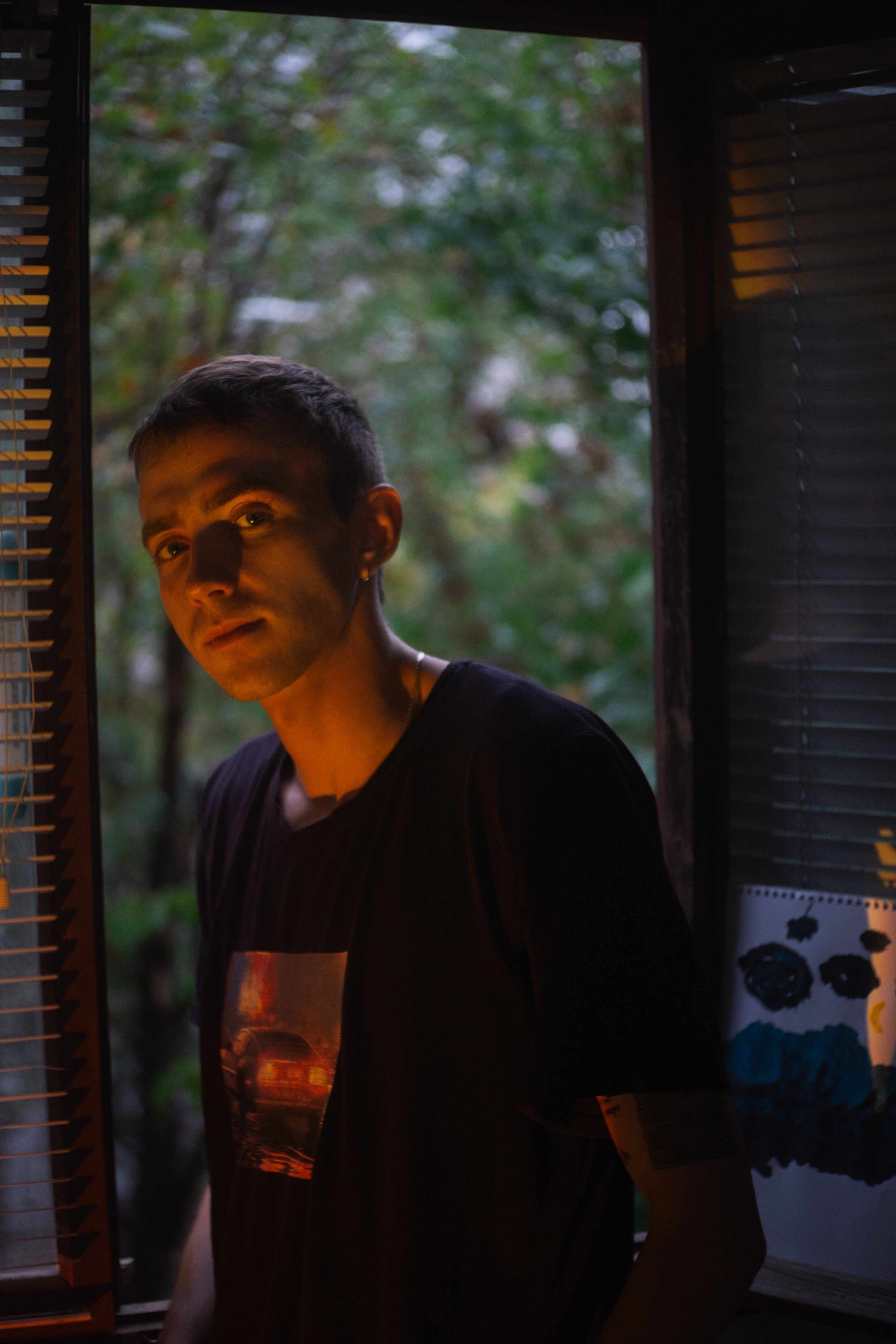 Young man standing by window at twilight with natural background.