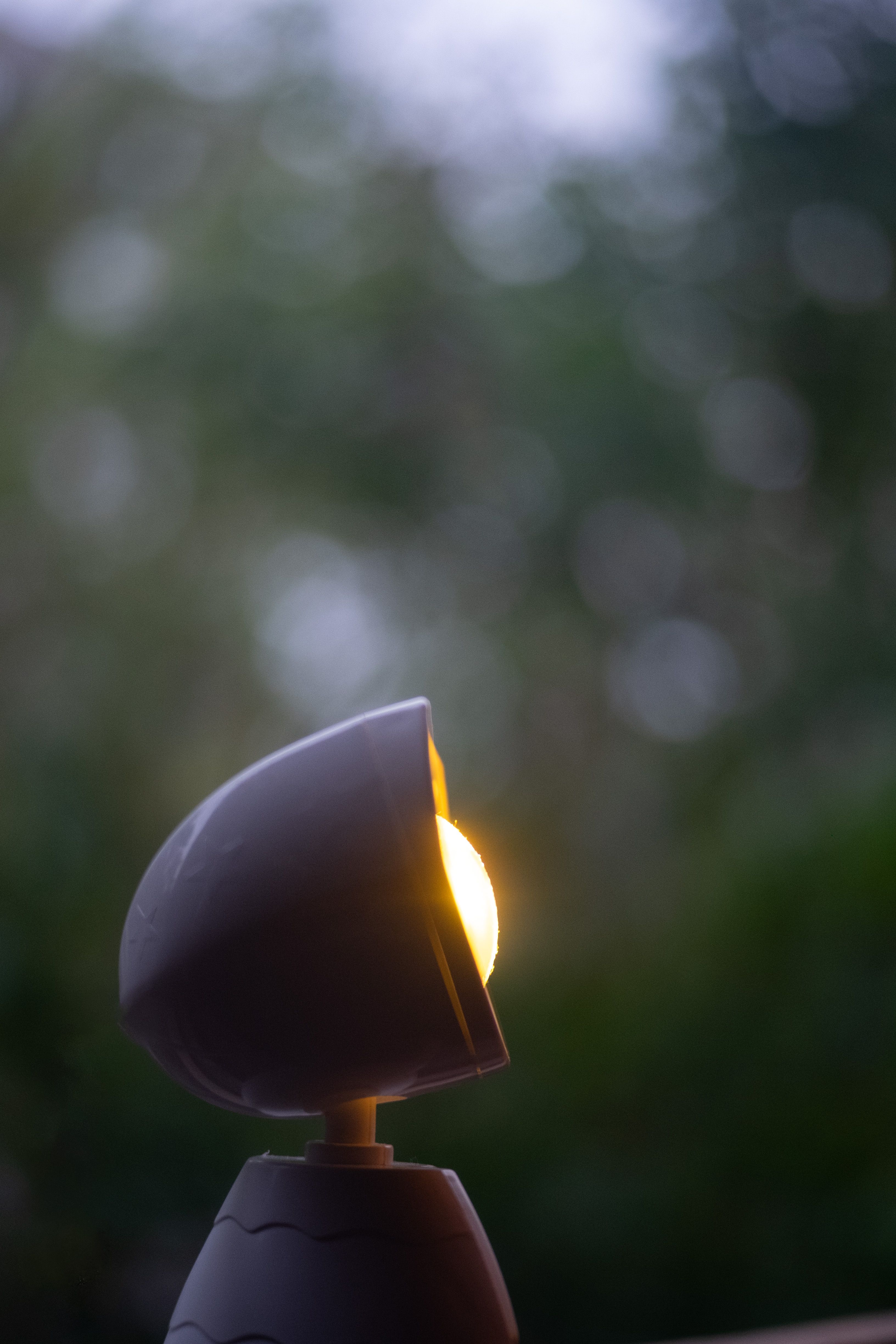 A modern outdoor lamp glowing softly amid blurred, lush green foliage.