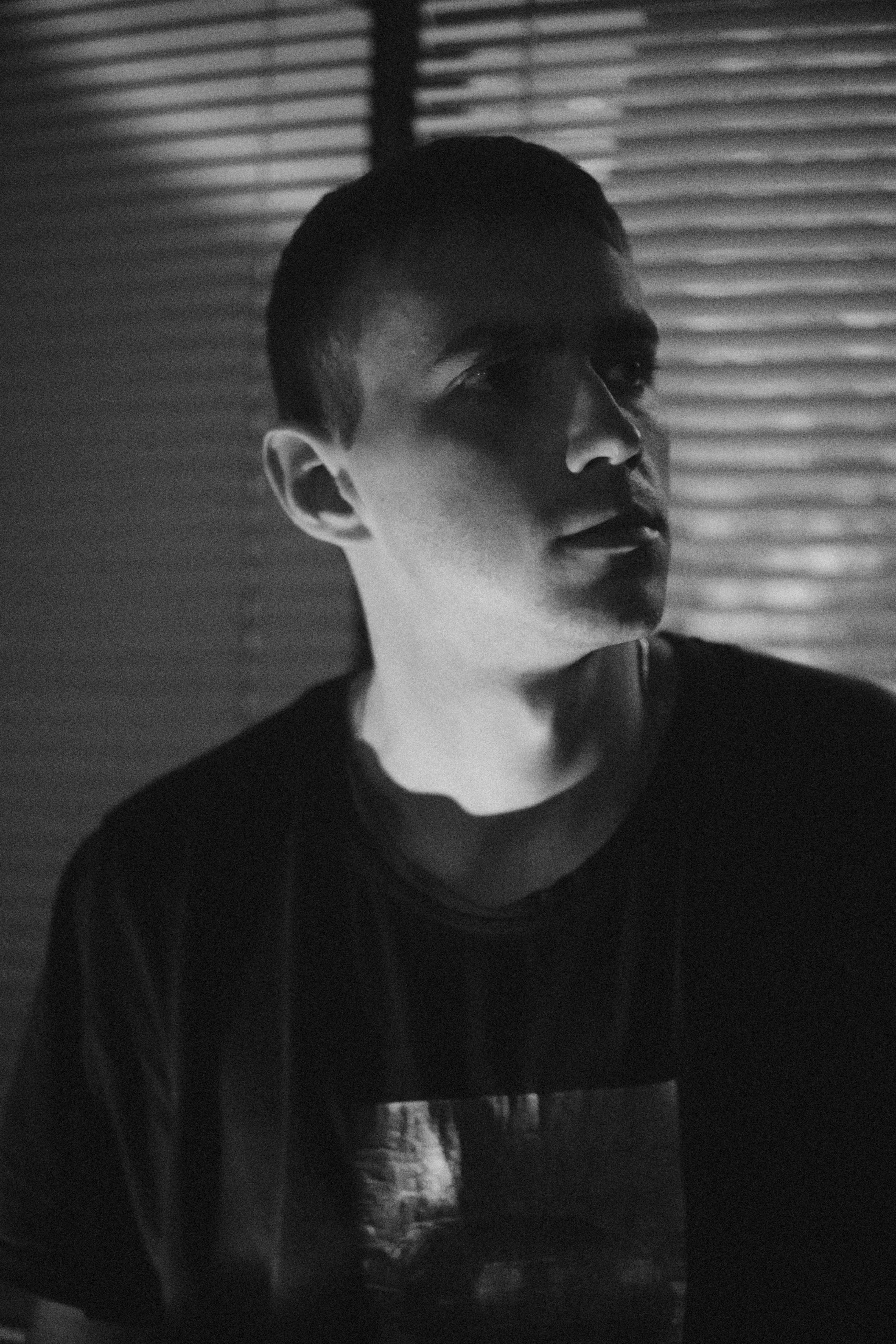 Dramatic black and white portrait of a man in shadowed indoor setting.