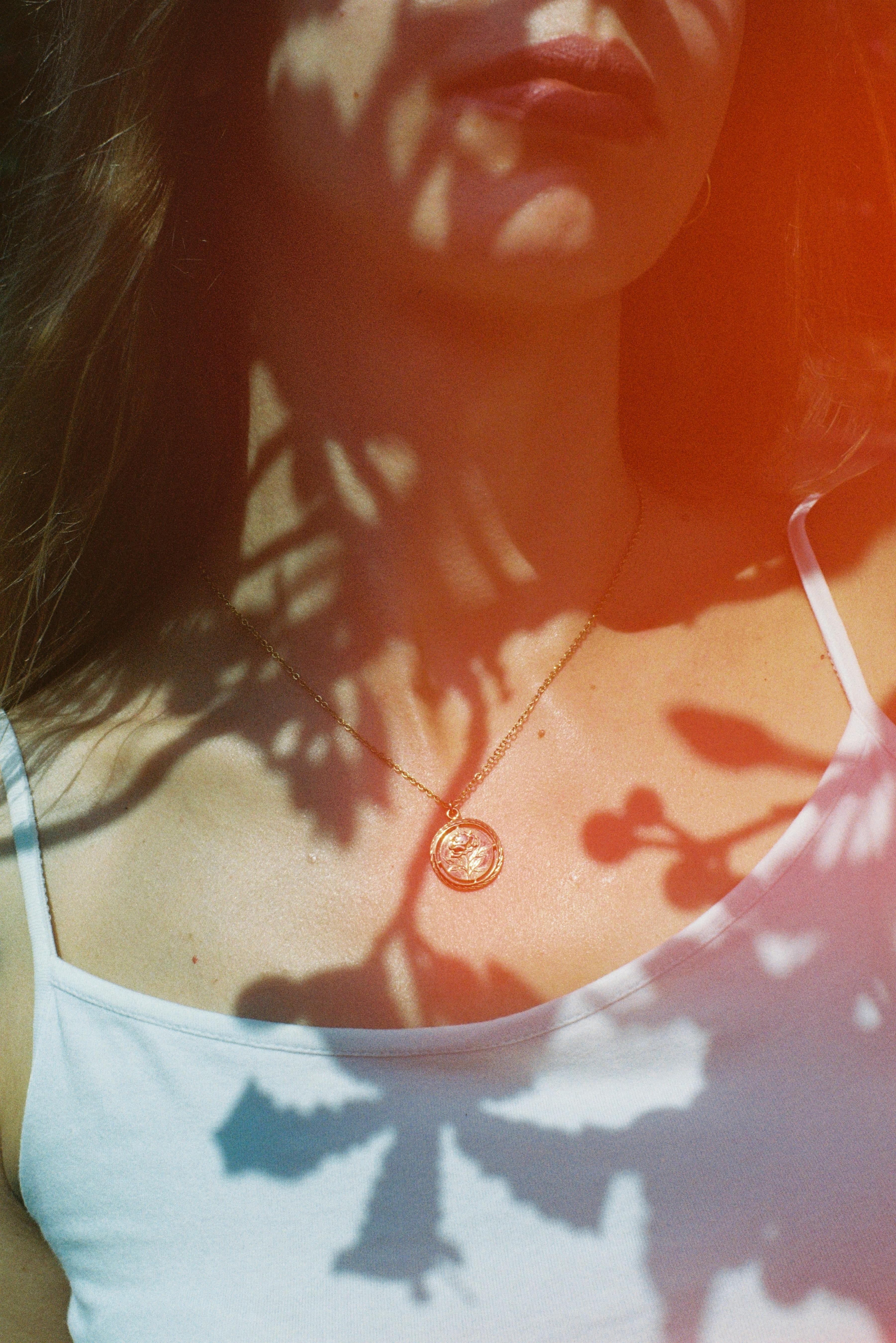 A woman wearing a necklace casts artistic shadows in natural light, evoking a sense of mystery.
