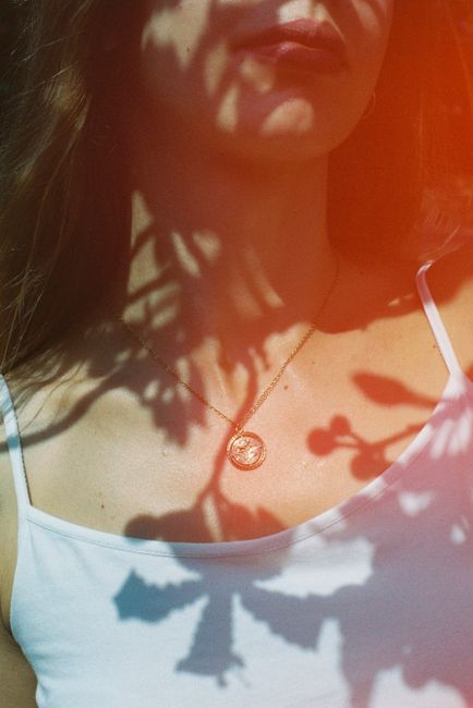 A woman wearing a necklace casts artistic shadows in natural light, evoking a sense of mystery.