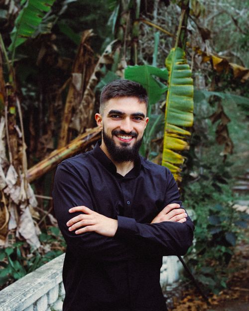 Free Young man in black shirt smiling with arms crossed in a lush tropical garden setting. Stock Photo