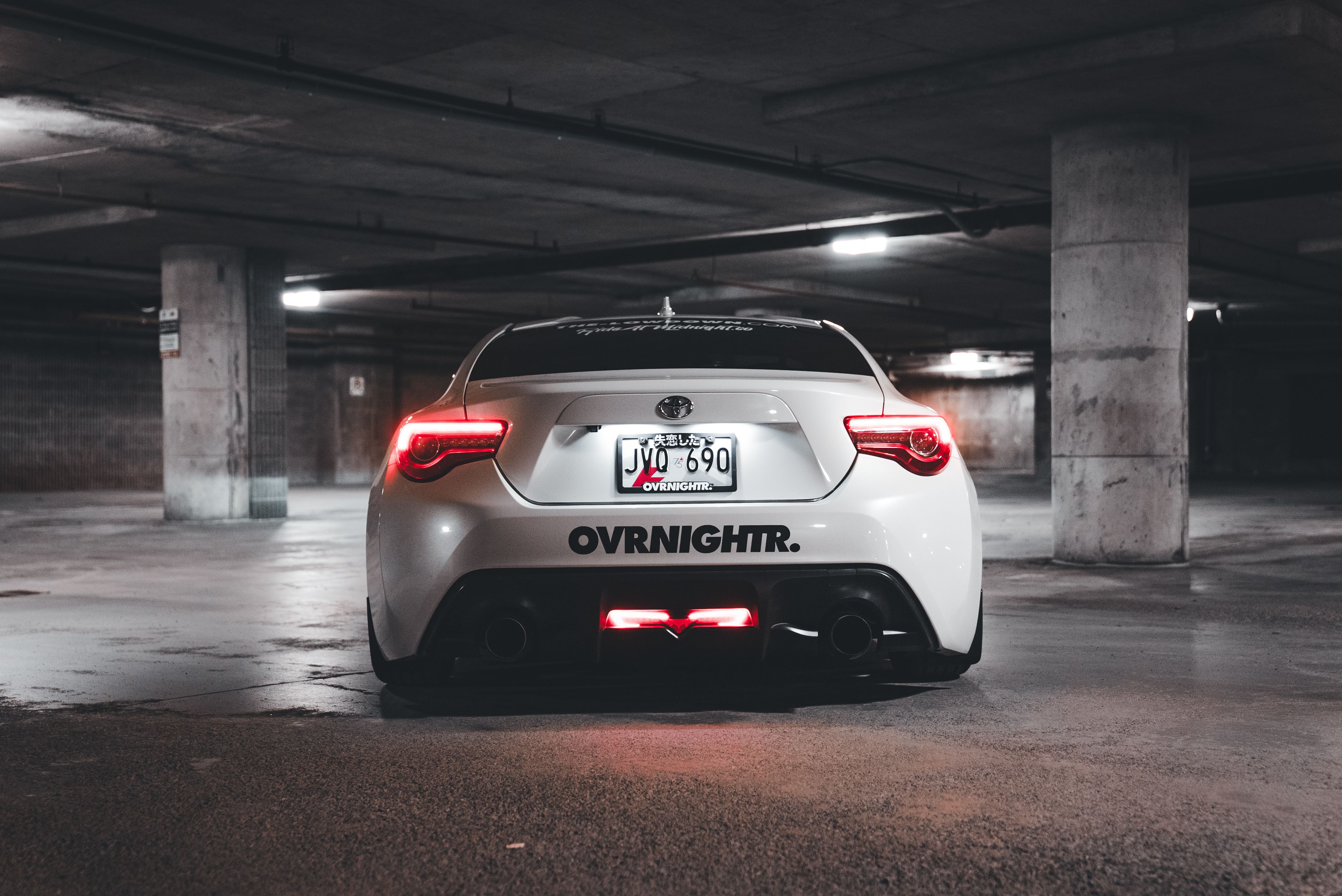 A sleek white sports car parked in a dimly lit underground garage, highlighting its rear view.