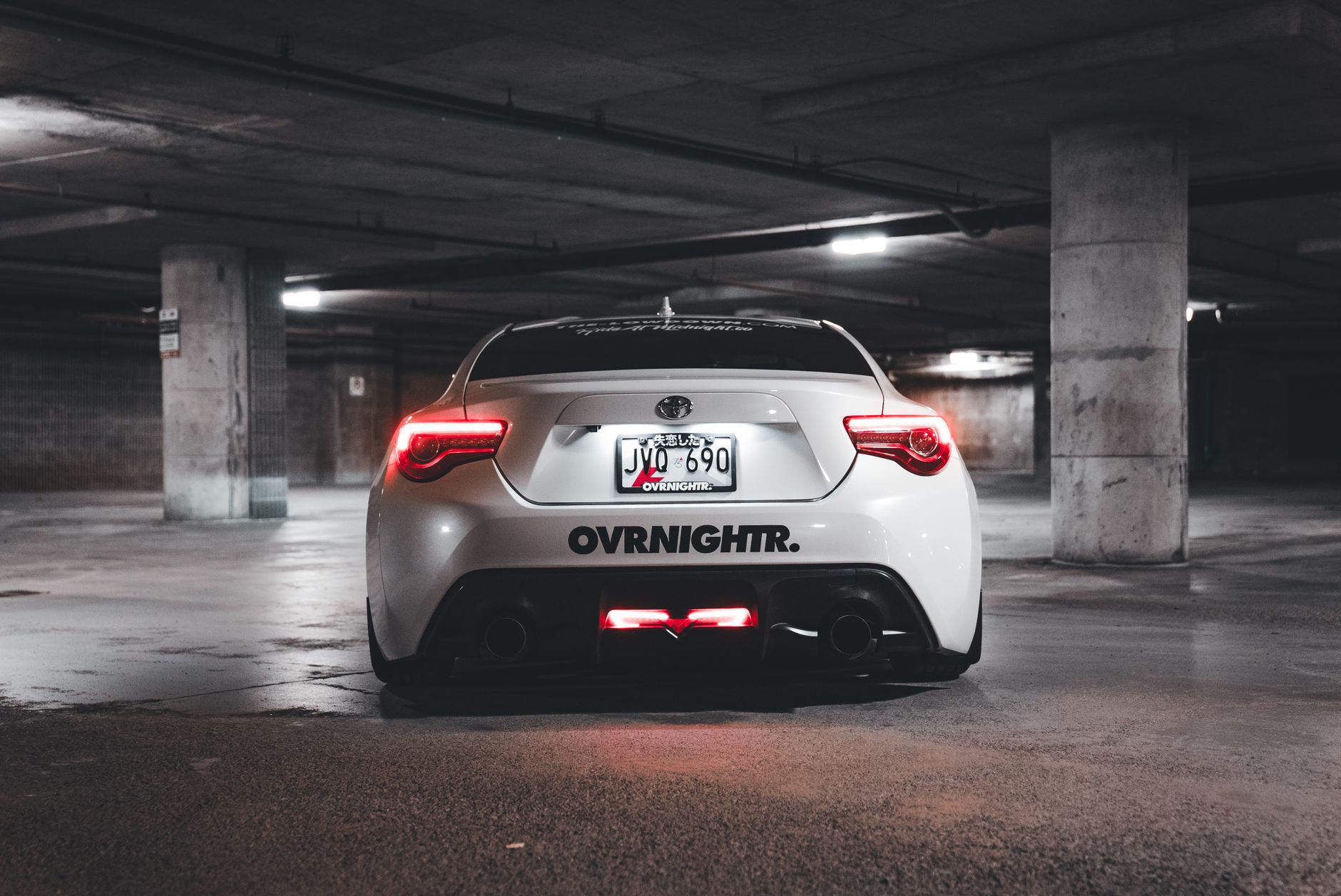 A sleek white sports car parked in a dimly lit underground garage, highlighting its rear view.