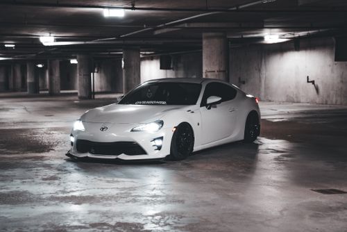 Free White sports car with headlights on inside a dim urban parking garage, showcasing modern design. Stock Photo