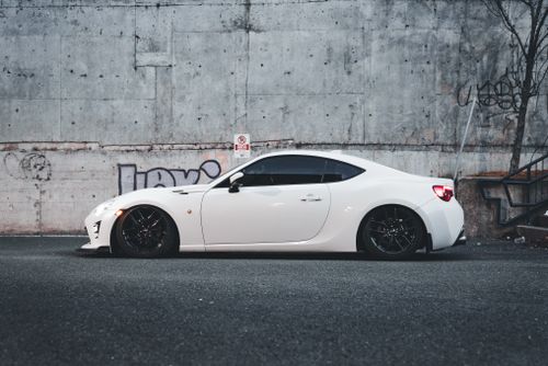 Free A stylish white sports car parked against a graffiti-lined concrete wall in an urban environment. Stock Photo