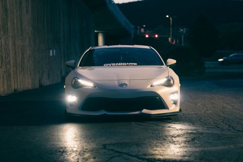 Free A sleek white sports car with headlights on, captured at night under a bridge. Stock Photo