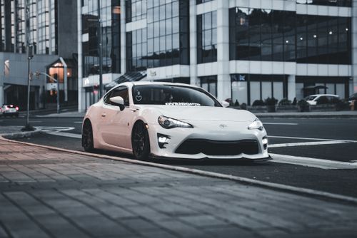 Free White sports car parked on city street with modern glass buildings in background. Stock Photo