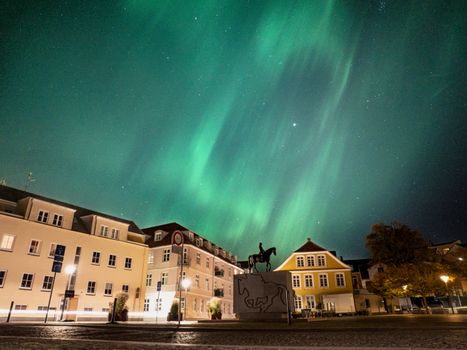Breathtaking view of the Northern Lights over Sønderborg, Denmark, with historic buildings and a night sky.