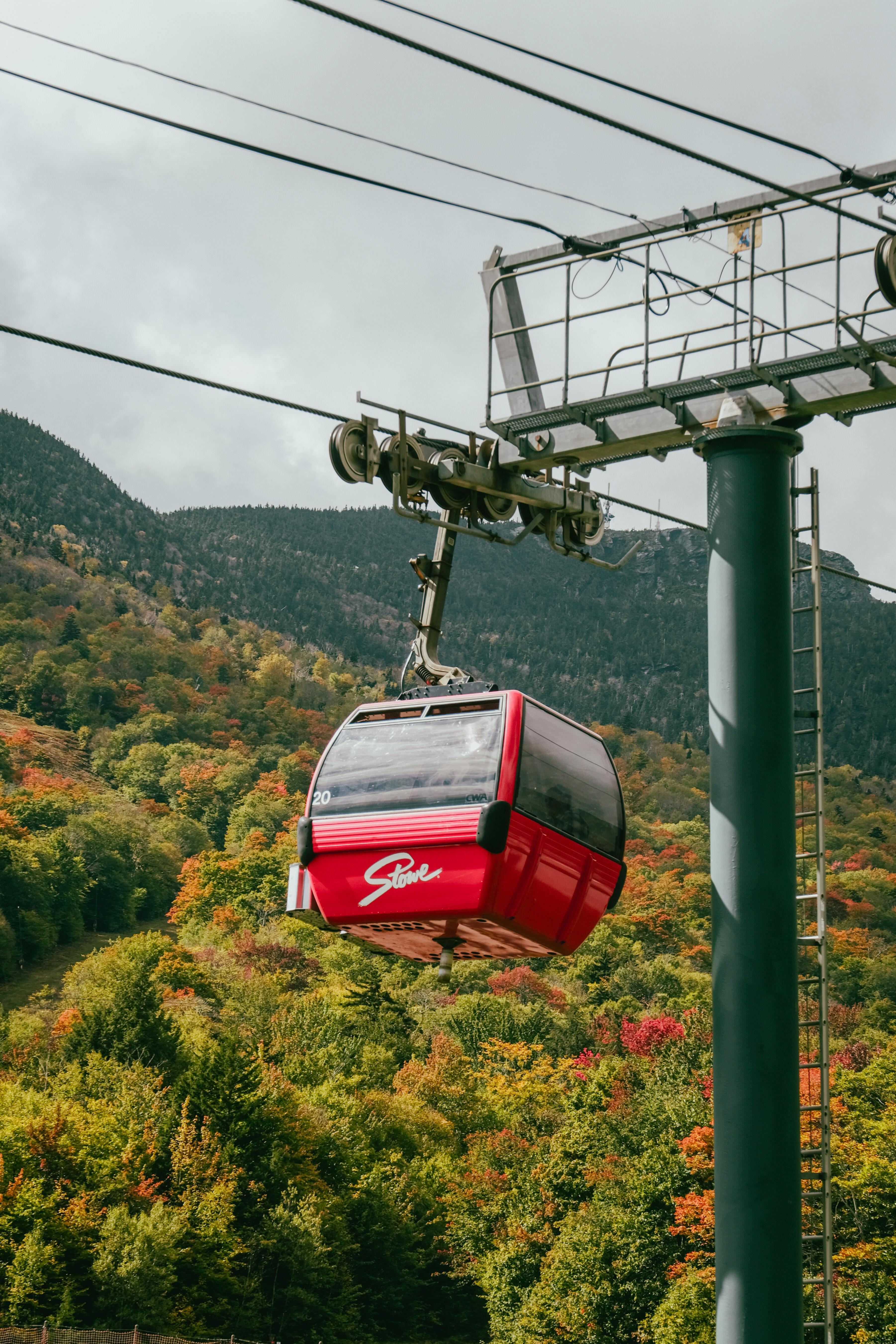 Vibrant red gondola travels through autumn foliage in a mountainous region, capturing the beauty of seasonal change.