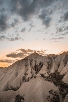 一位孤独的冒险家站在岩石山峰上，在壮观的日落天空下，捕捉到了探索的本质