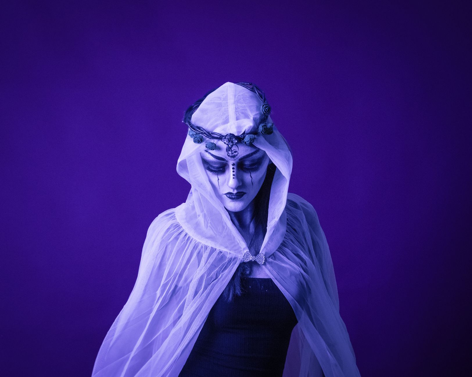 A woman in white veil with elaborate face paint on a purple background.