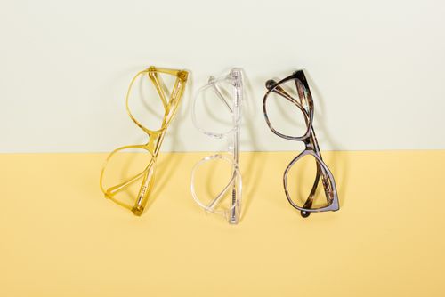 Free Three pairs of fashionable eyeglasses arranged on a pastel yellow and off-white background, showcasing minimal design. Stock Photo