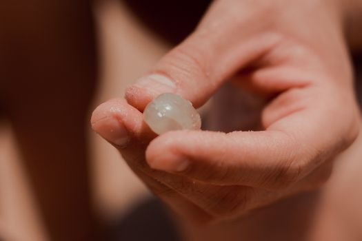 A close-up shot of a hand holding a translucent sea marble on a sunny beach in Aracati, Brazil.