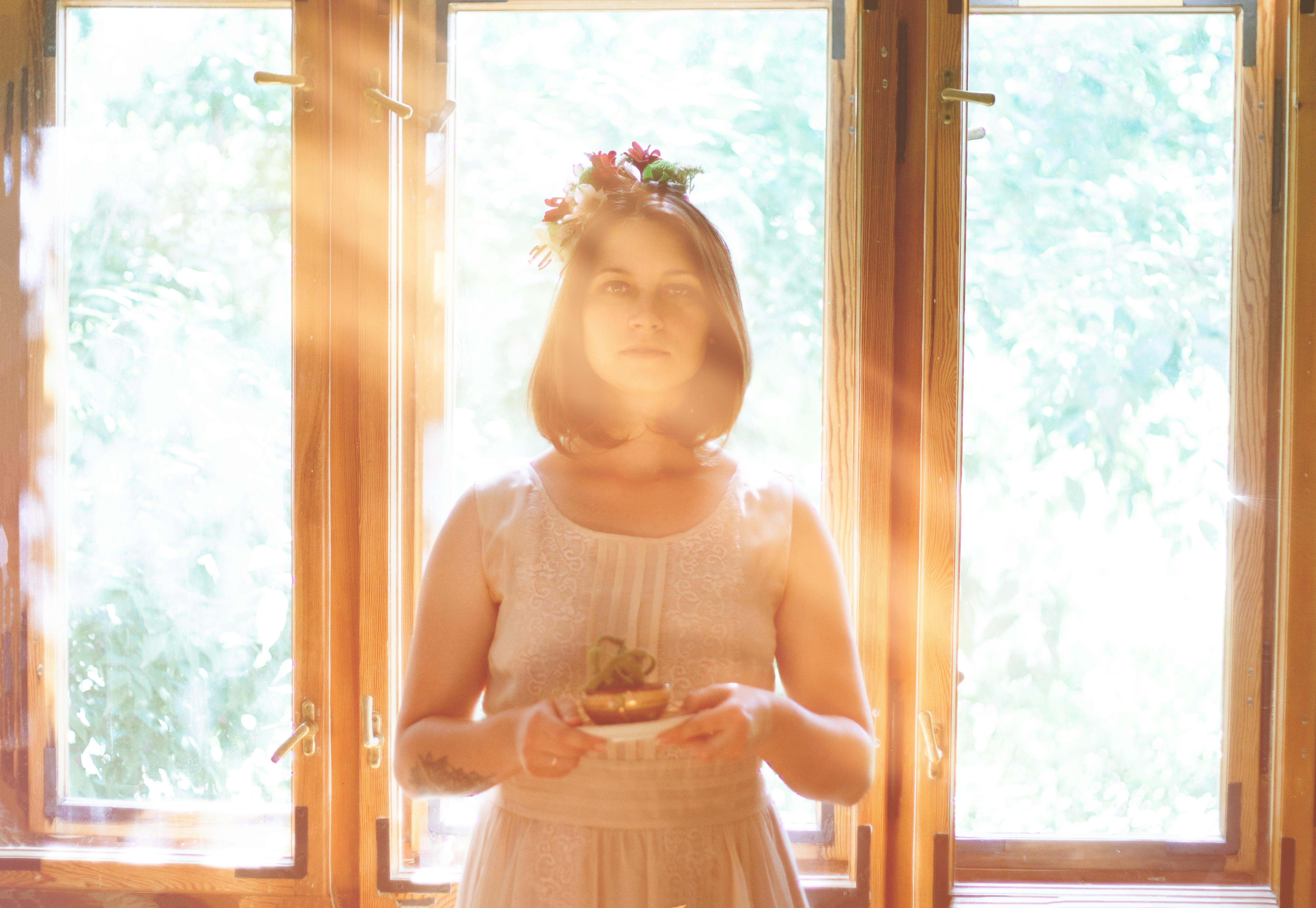 Woman stands in sunlight holding a small plant, surrounded by warm window light.