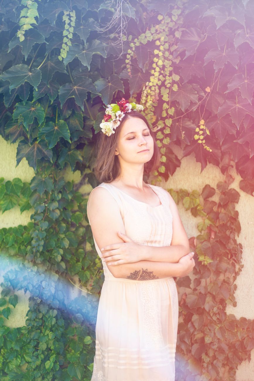 Serene portrait of a woman outdoors in a floral crown and dress against a green leafy background.