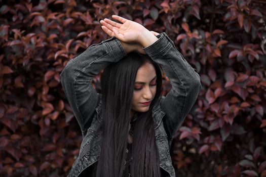 一位留着深色长发、穿着牛仔夹克的女性在墨西哥户外充满活力的绿叶背景下摆姿势