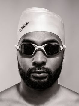 Close-up black and white portrait of a male swimmer wearing goggles and swim cap.