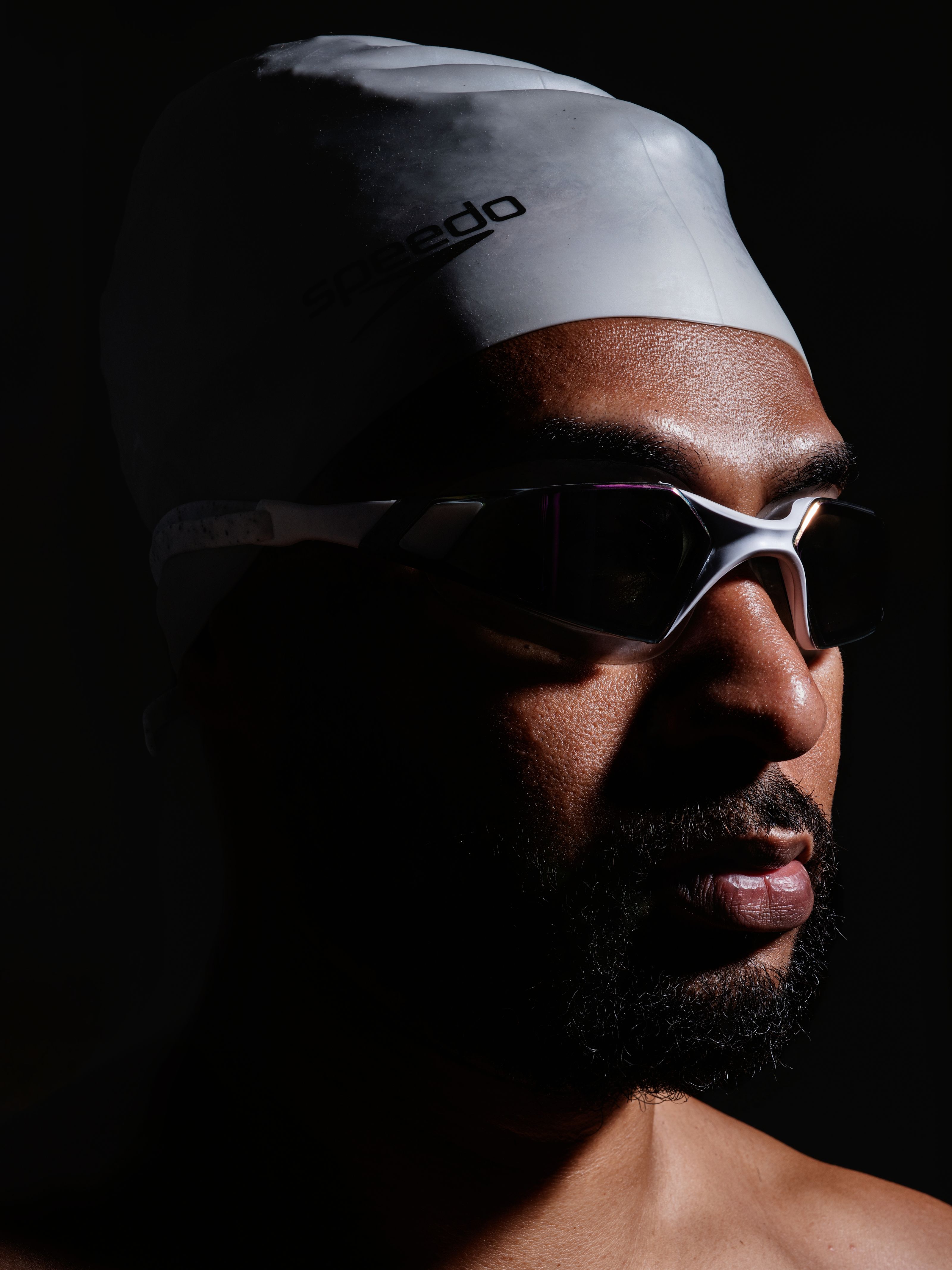 Retrato de um atleta usando touca de banho e óculos em iluminação dramática.