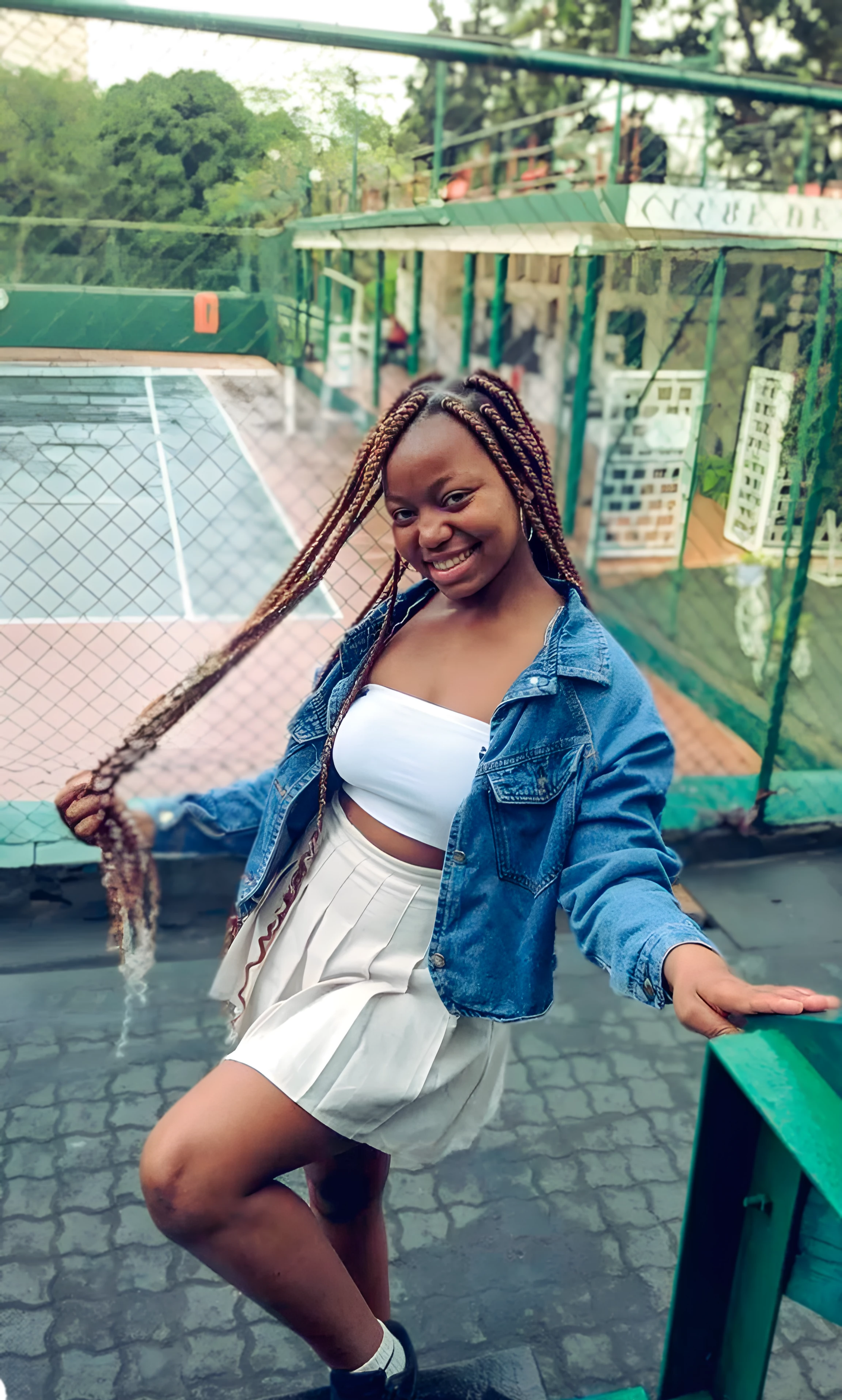 Smiling young woman in casual outfit posing at an outdoor tennis court, exuding joy and confidence.