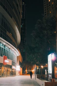 A lone figure walks along the illuminated streets of Dubai Marina at night, showcasing modern architecture.