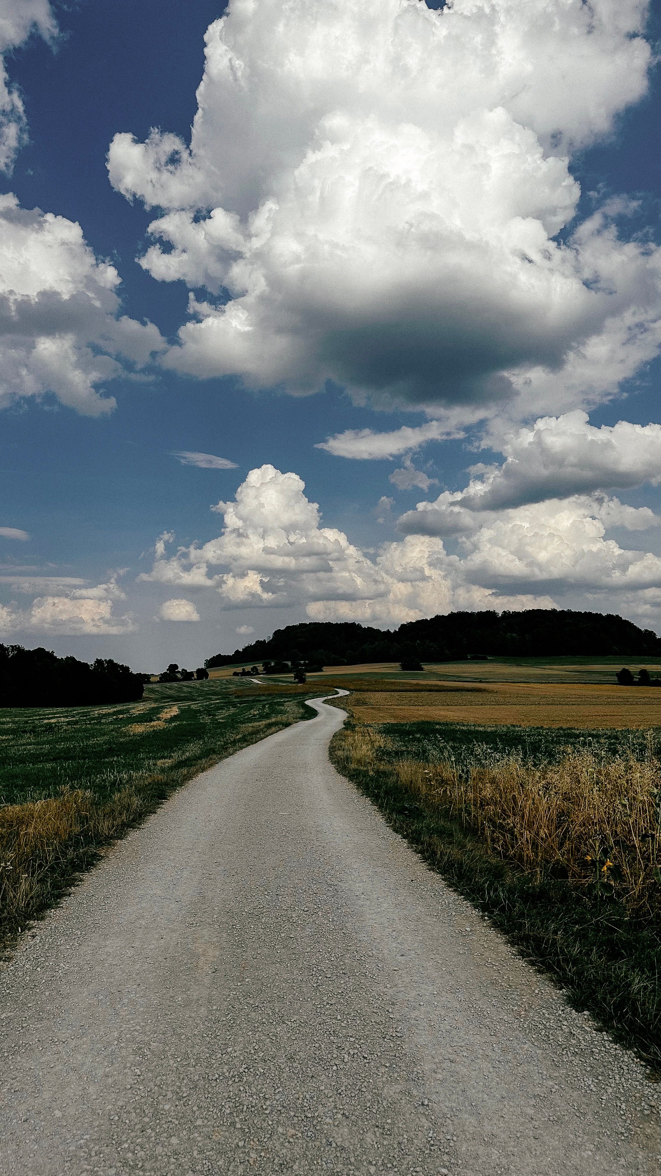 Winding dirt road through the countryside under expansive, dramatic clouds.