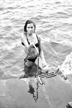 Black and white photo of a woman at the water's edge holding a railing.