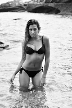 Black and white photo of a woman in swimwear standing in the ocean.