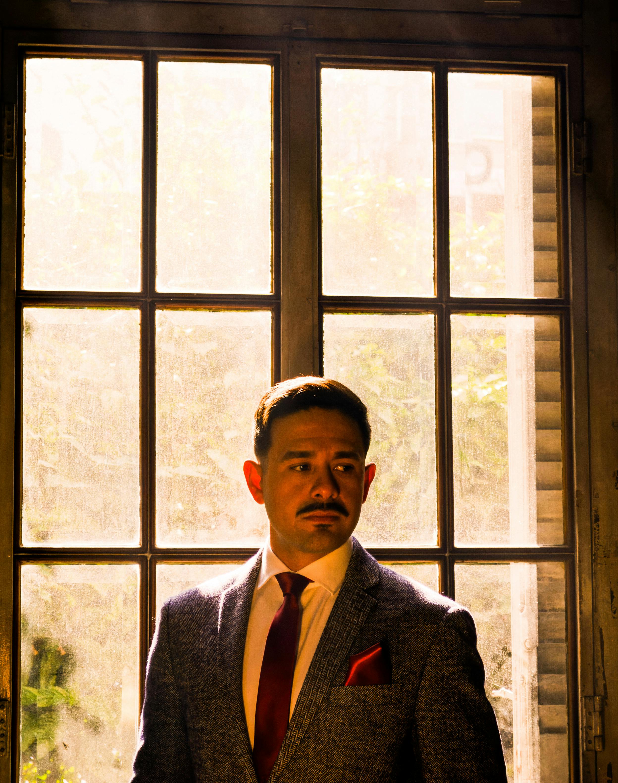 A man in a stylish suit stands by a sunlit window, creating a warm, sophisticated ambiance.