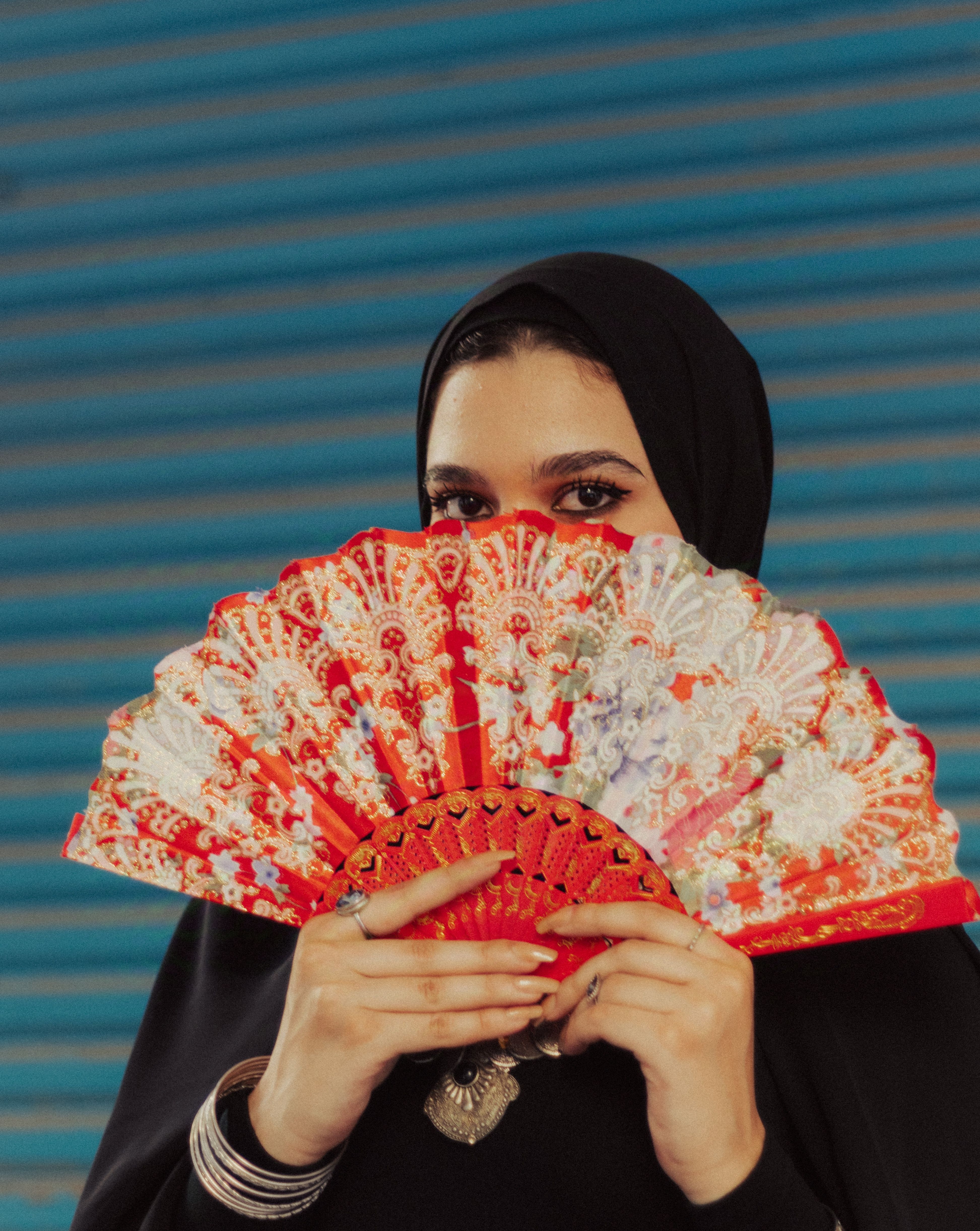 Woman in hijab holding a colorful fan, creating a mysterious look.
