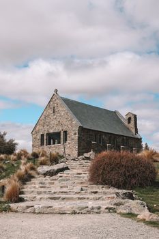A picturesque stone church with rugged steps in a mountain landscape under a cloudy sky.