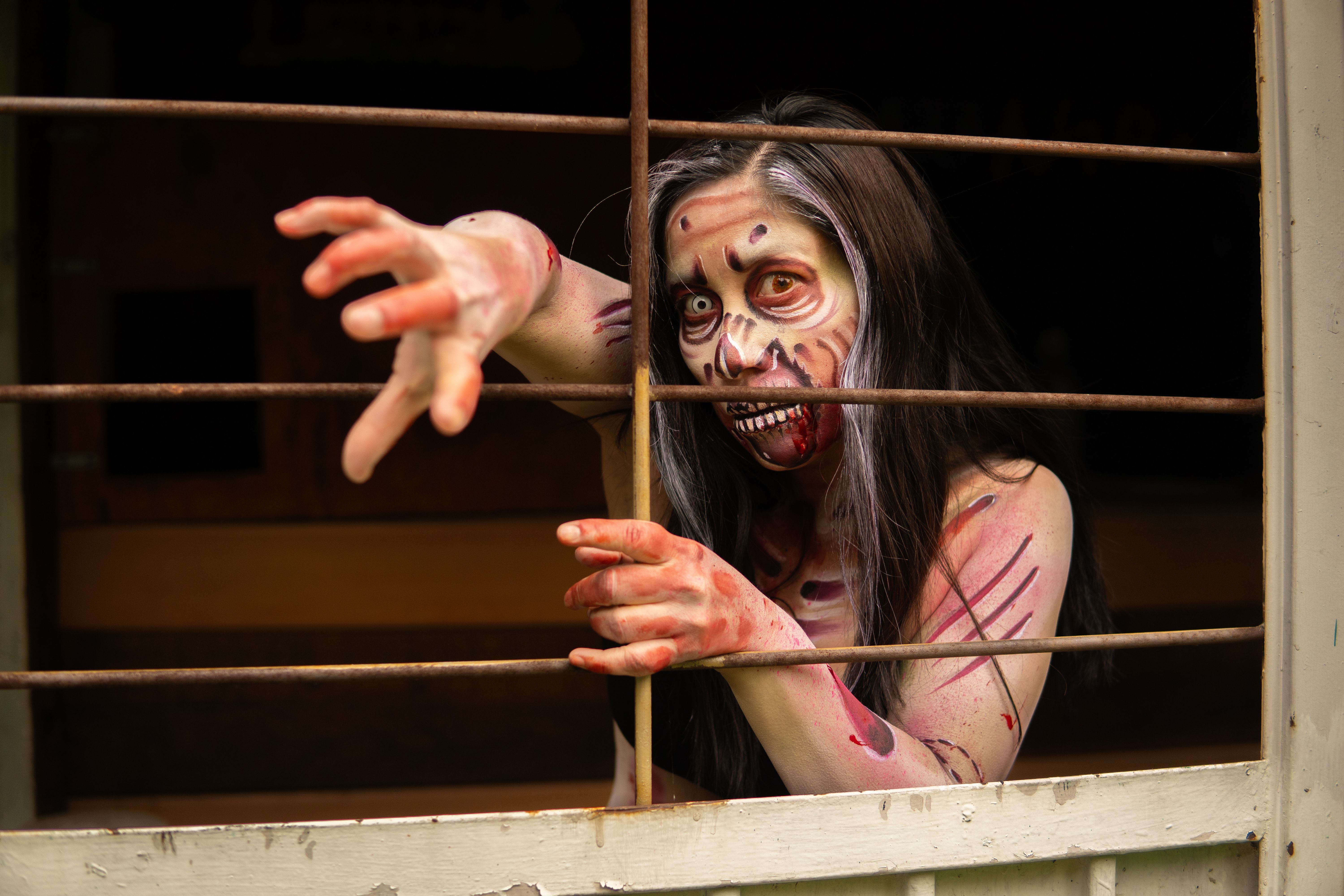 Terrifying zombie cosplay with Halloween makeup, reaching through a window.