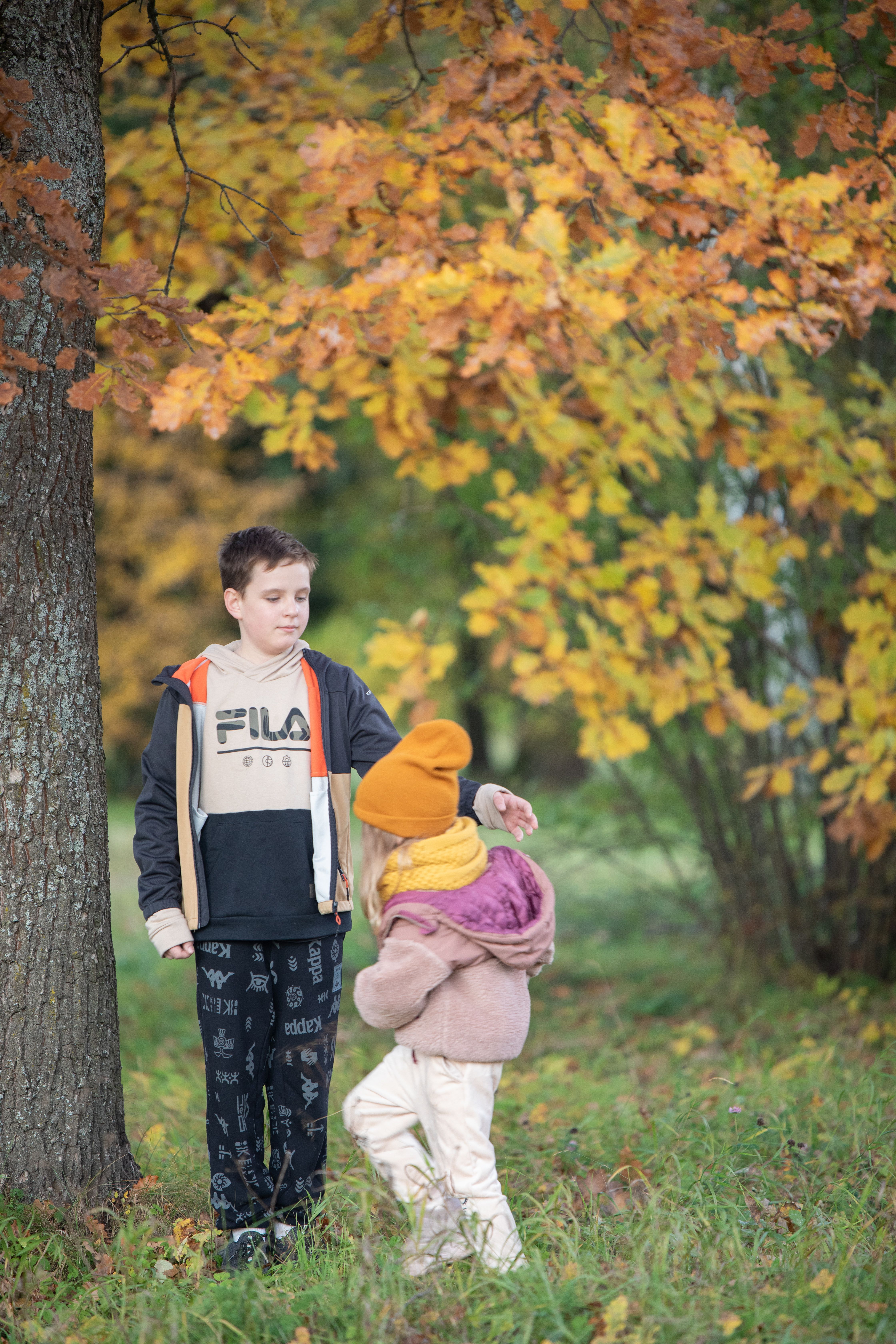 Two children playing under colorful autumn leaves in a park setting.