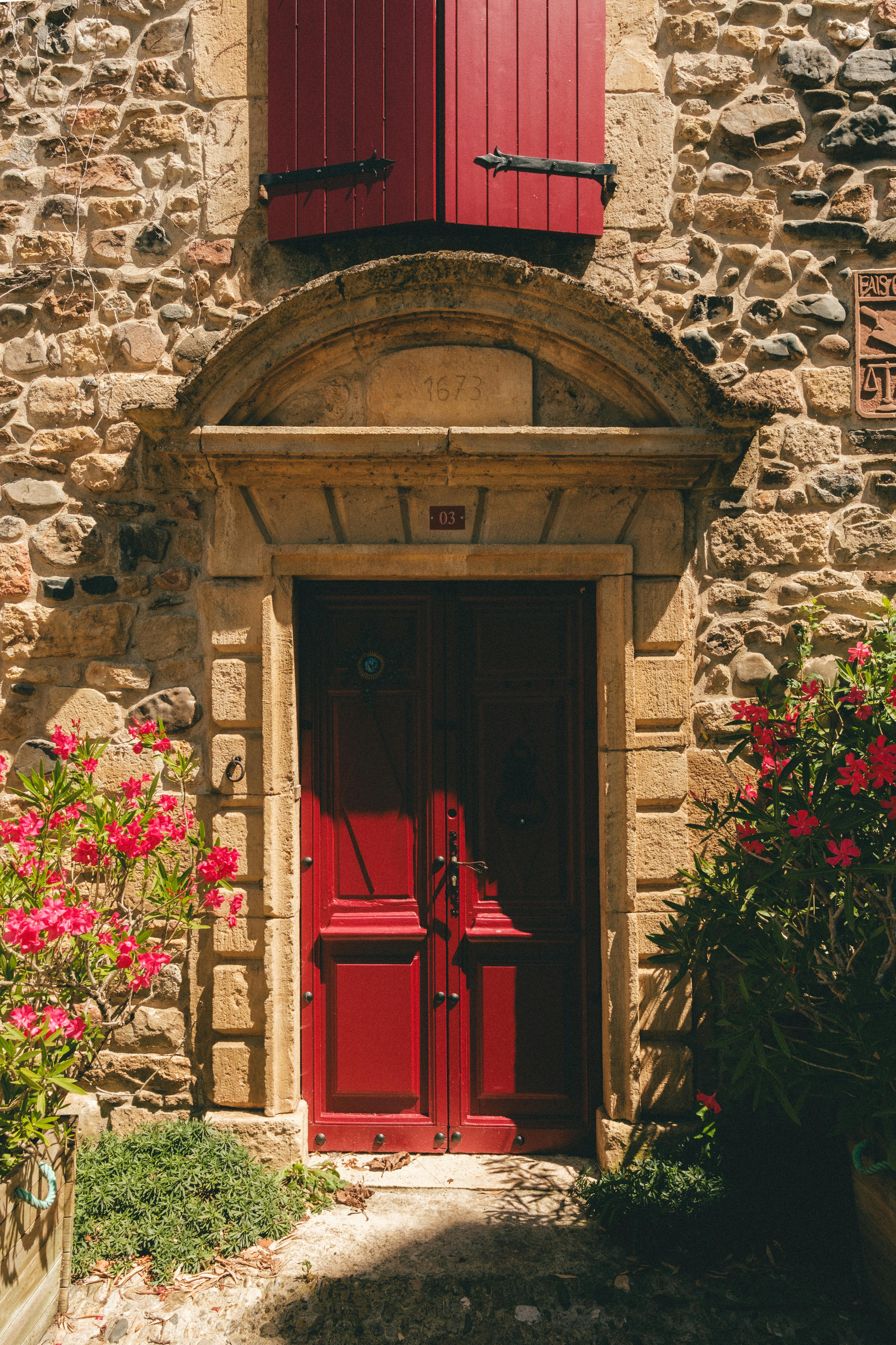 Charming stone house in Saint-Chély-d'Aubrac with vibrant red door and flowers.