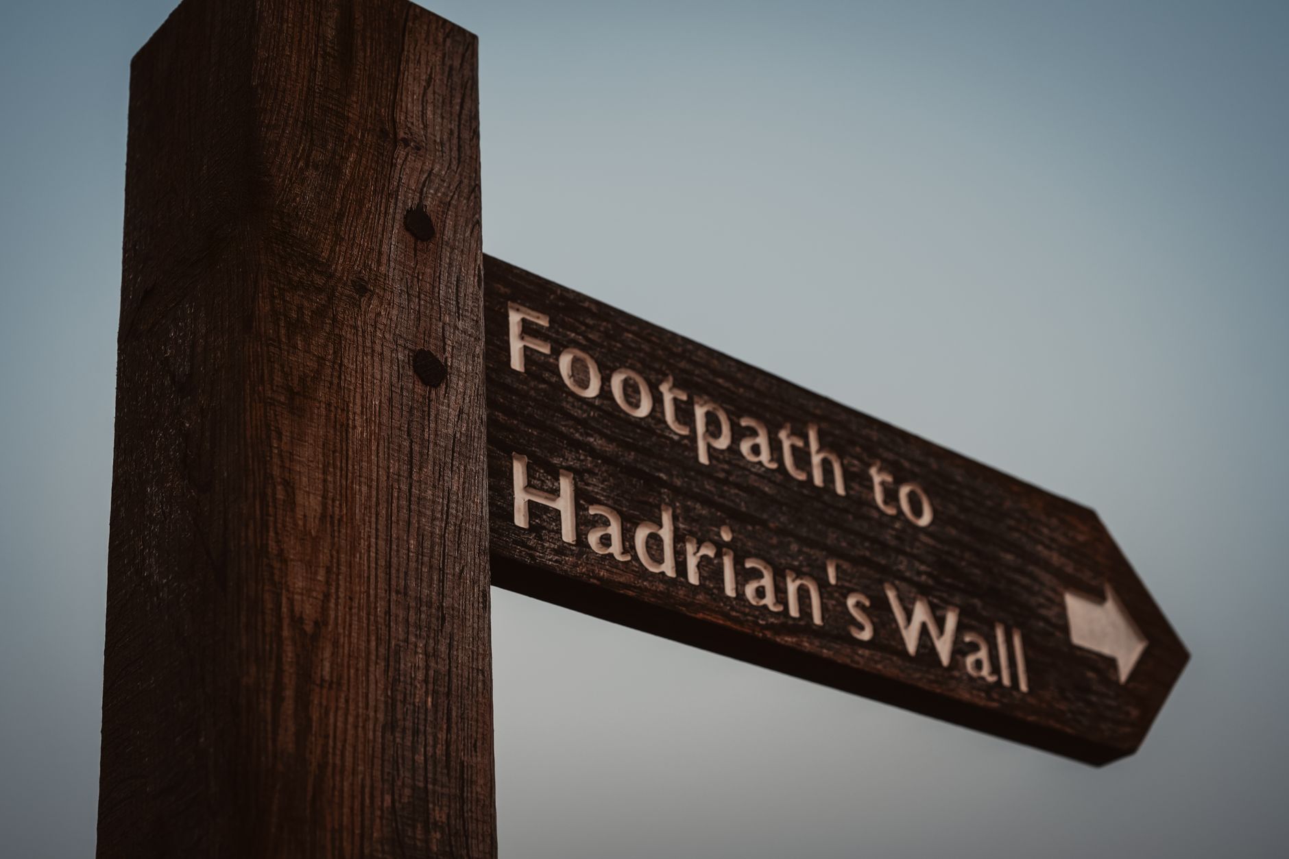 Wooden footpath sign pointing to Hadrian's Wall through open Northumberland moorland