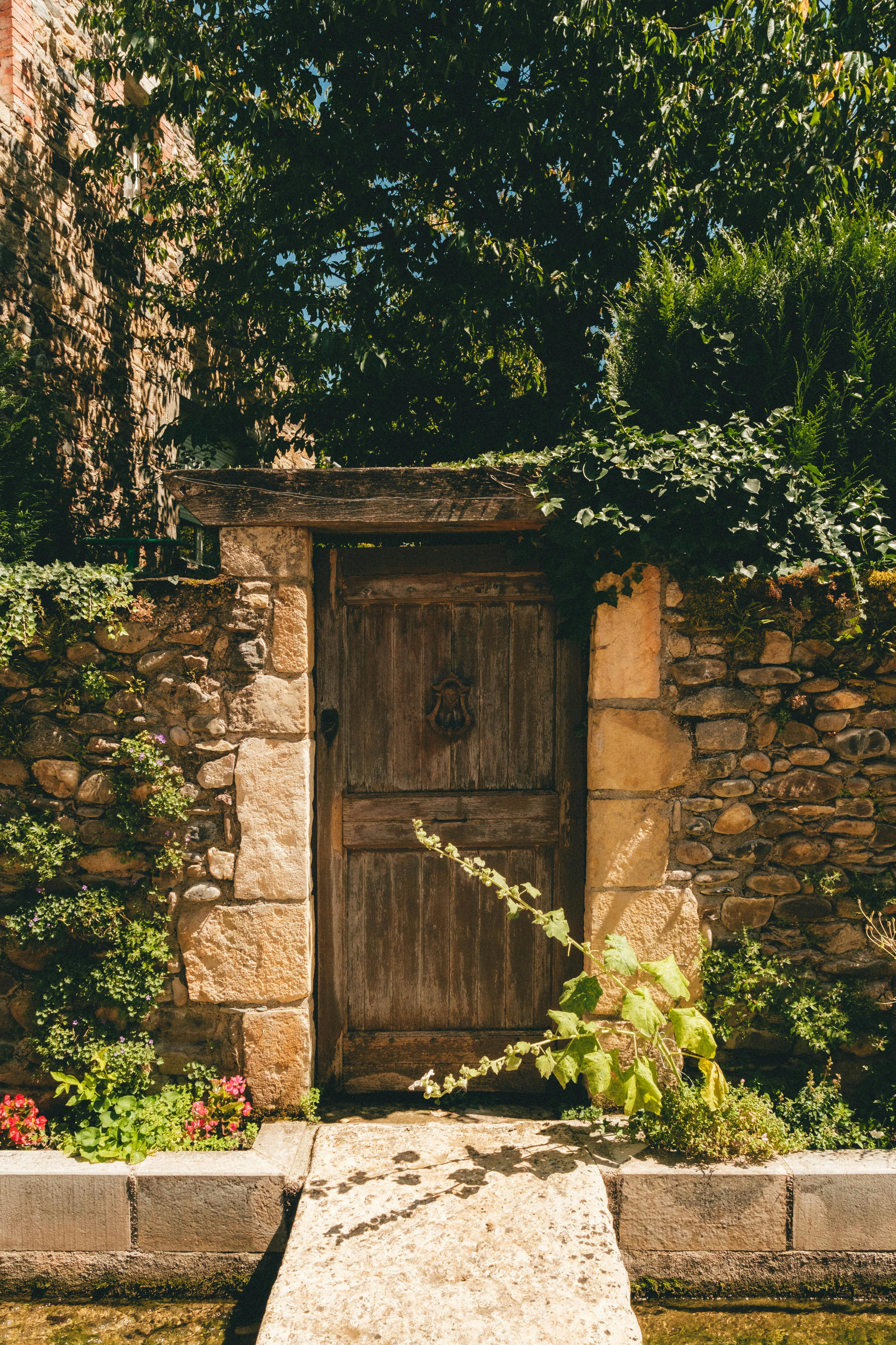 Charming rustic stone wall with a weathered wooden door, lush foliage, and vibrant flowers.