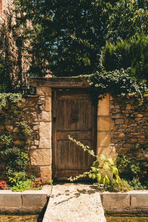 Free Charming rustic stone wall with a weathered wooden door, lush foliage, and vibrant flowers. Stock Photo