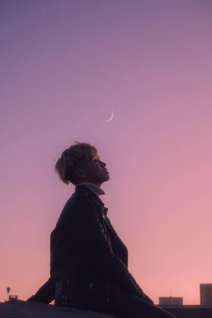 Silhouette of a person at twilight with crescent moon above San Francisco skyline.