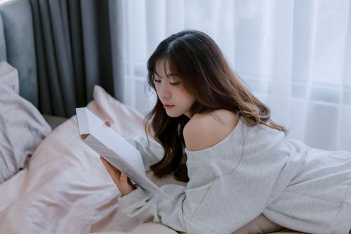 Free A young woman in a cozy setting is absorbed in reading a book by the window. Stock Photo