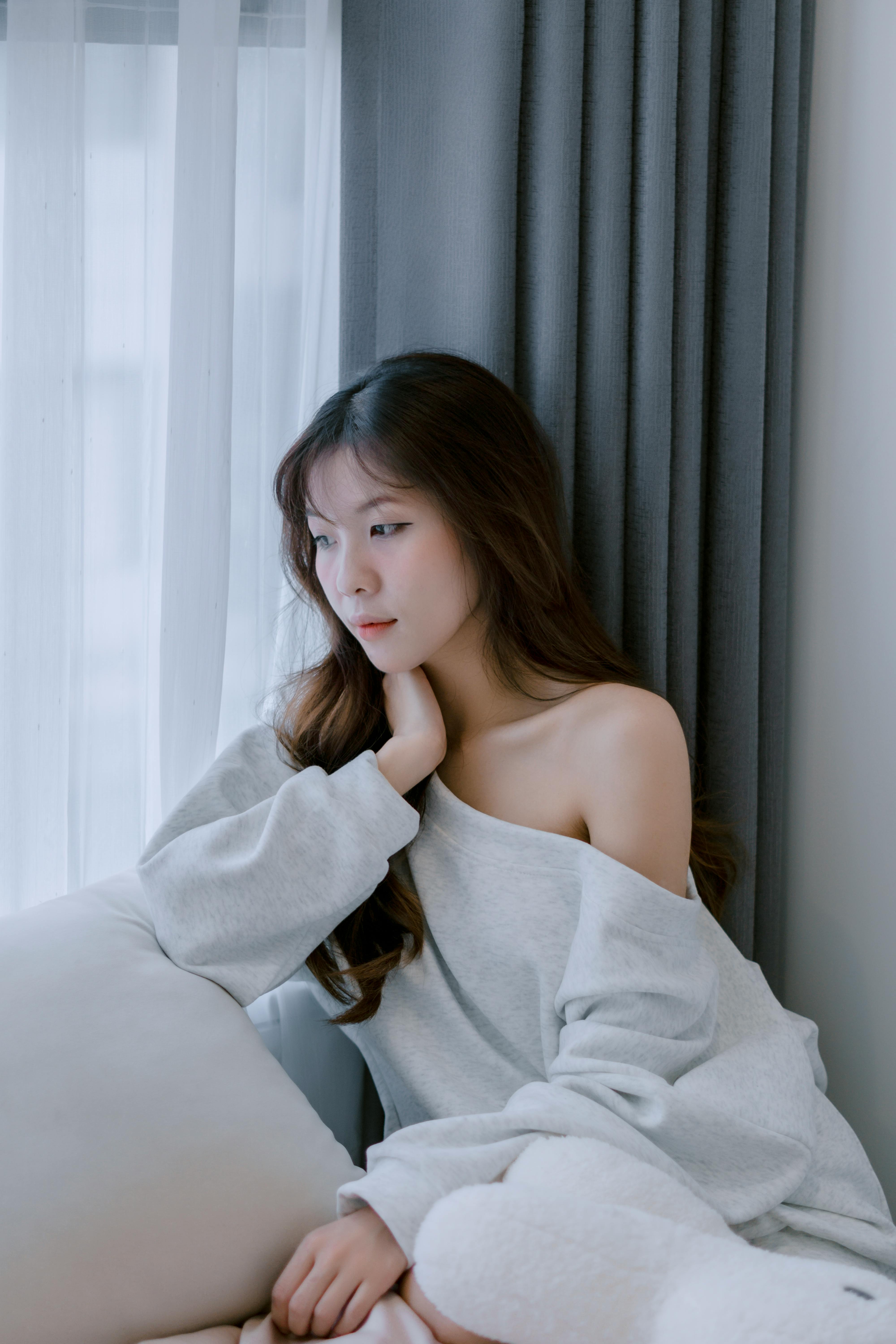 A contemplative young woman sitting by a window in a cozy setting.