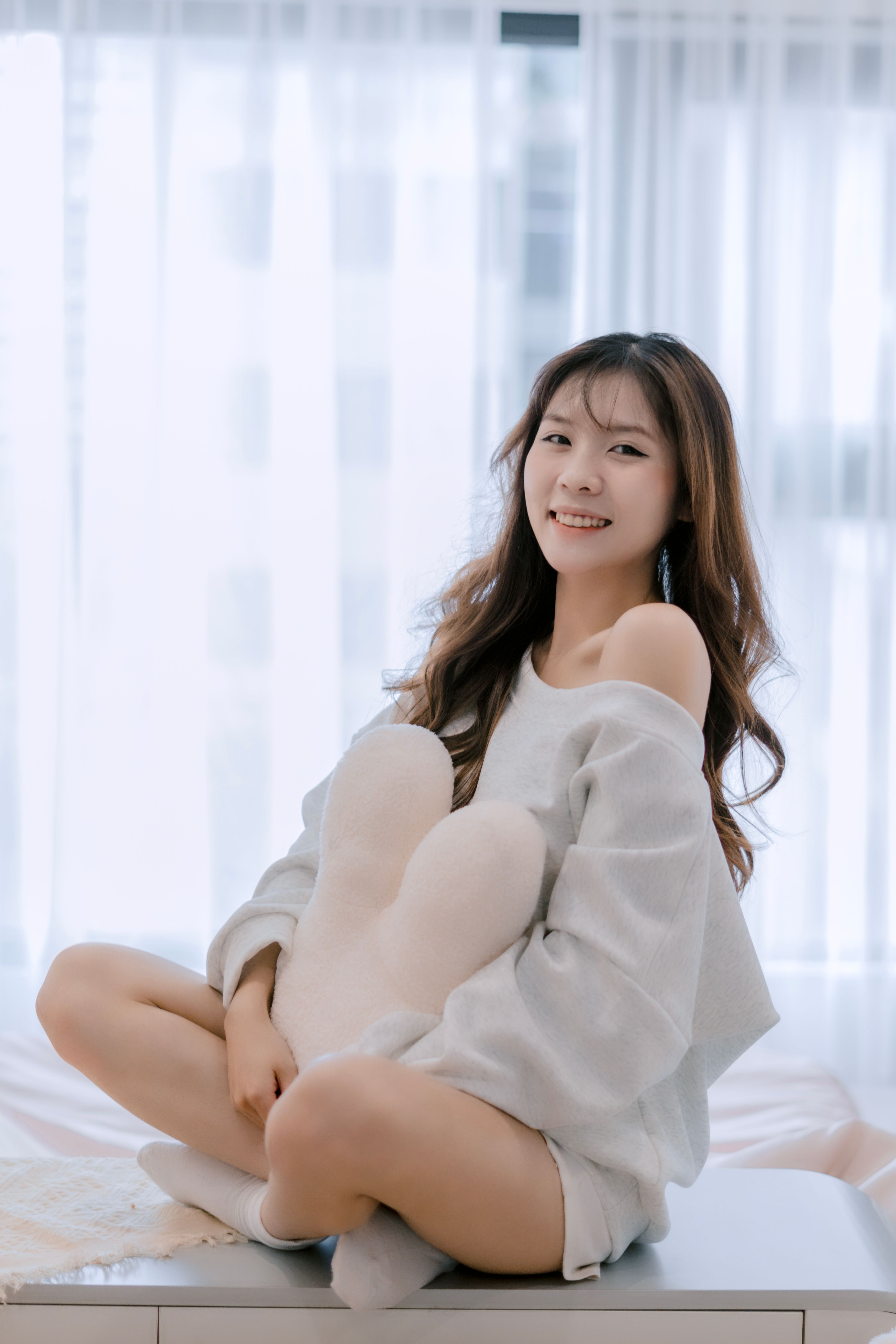 A woman sitting happily with a pillow in a bright indoor setting.