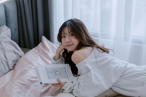 Free Young woman relaxing on bed reading a book in a cozy indoor setting. Stock Photo