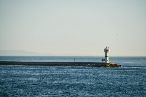 Free Lighthouse stands on a tranquil seascape with clear blue skies and calm waters. Stock Photo