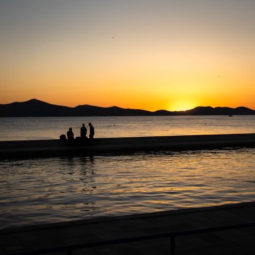 Free Silhouetted figures against a vibrant sunset over the sea in Zadar, Croatia, showcasing natural beauty. Stock Photo
