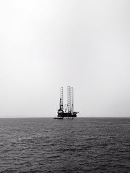 Black and white photo of an offshore oil rig in the ocean, conveying industrial isolation.